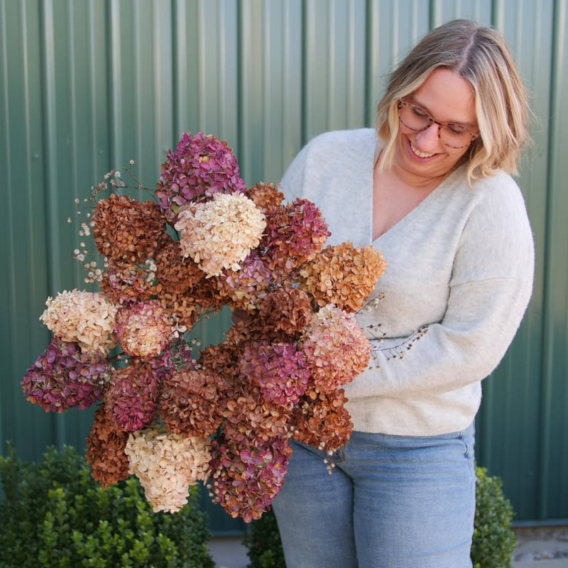 Blonde woman holding a handmade hydrangea wreath filled with pink, white, and brown hydrangeas
